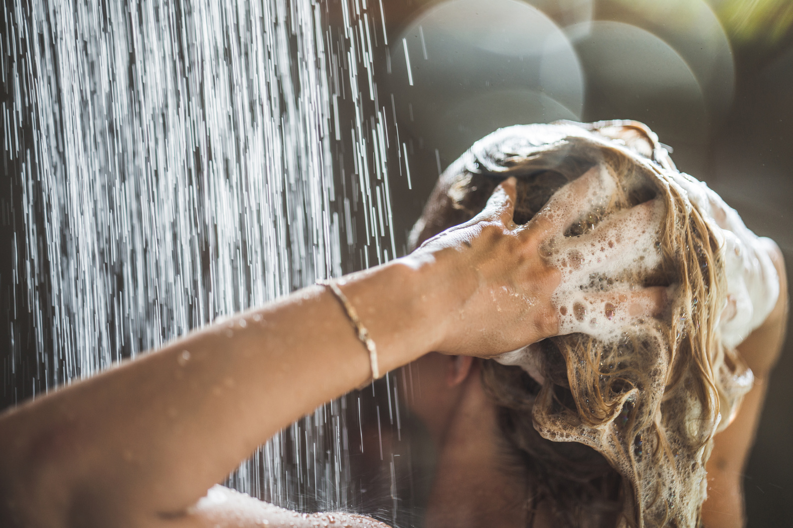 Woman washing her hair with shampoo under the shower.